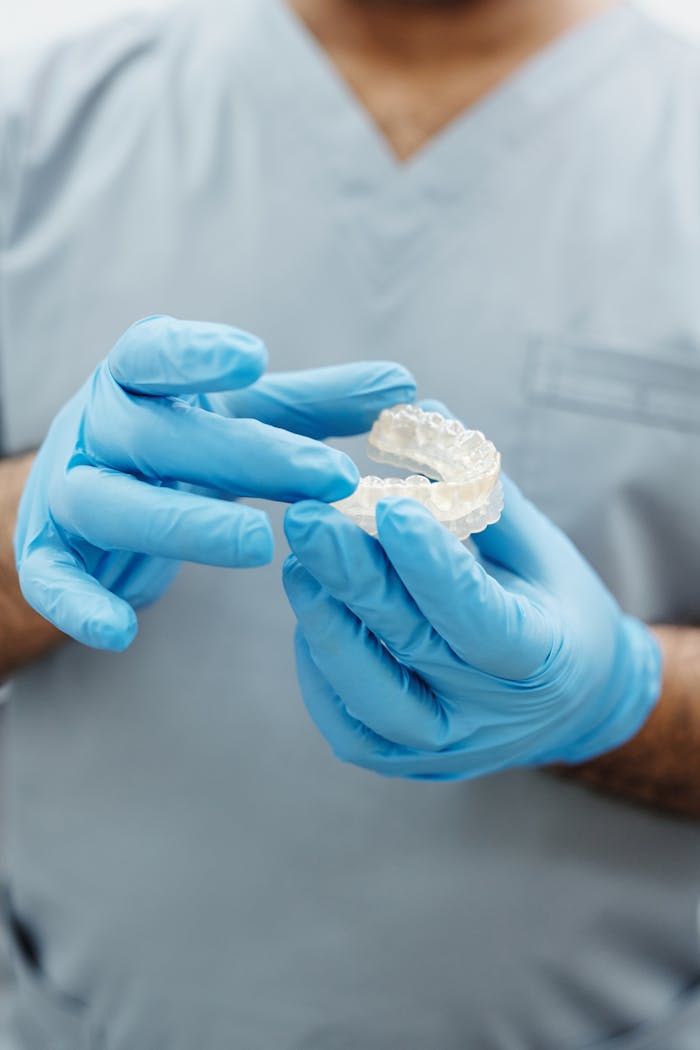 Dentist wearing blue gloves examining a dental mold in a clinical setting.